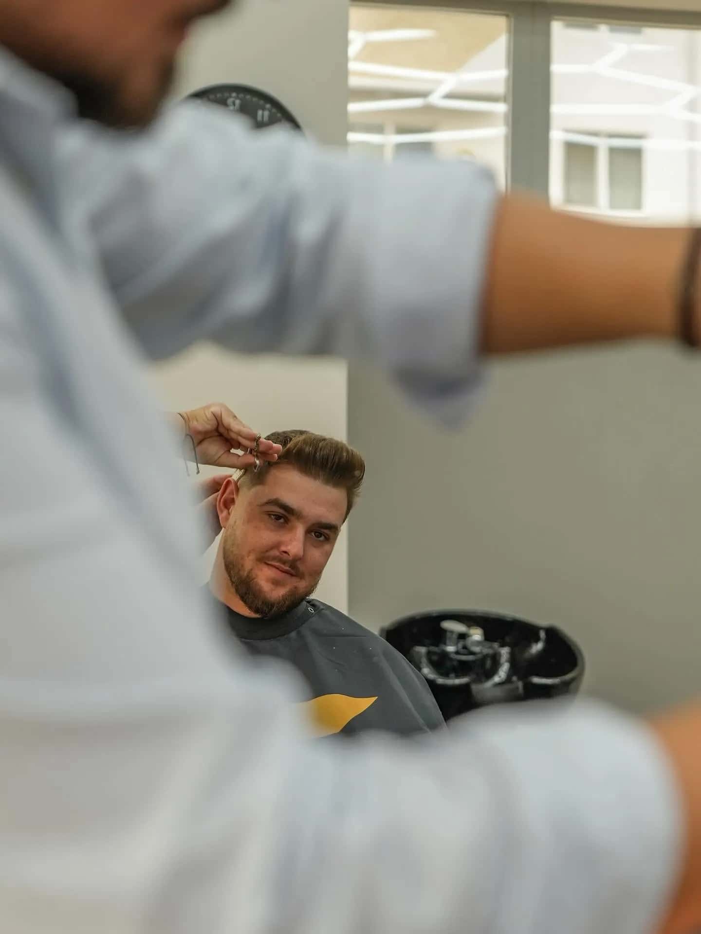 Client mulțumit la tuns, văzut pe lângă umărul frizerului