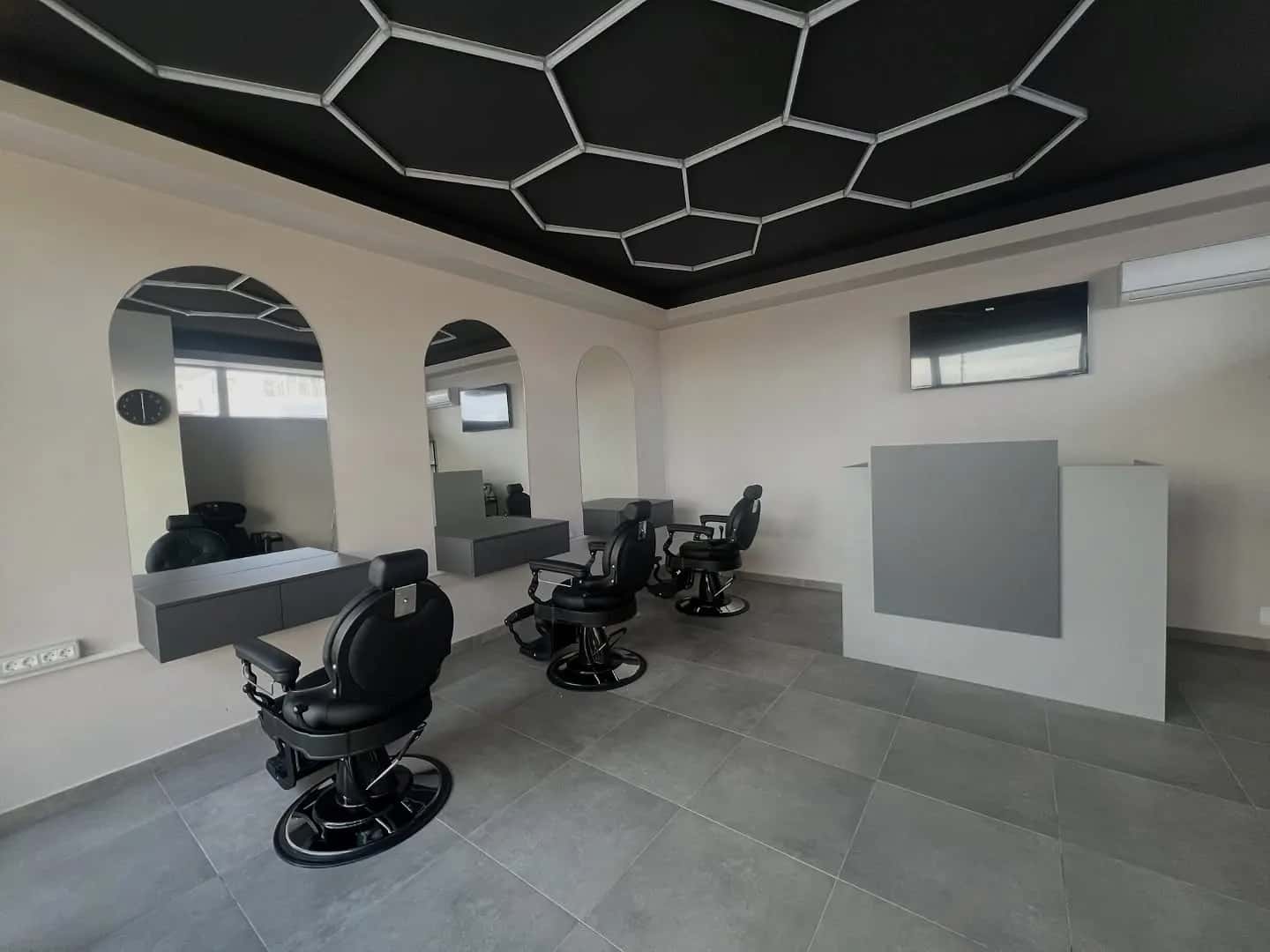 Interiorul R|B Barbershop: tavan cu LED-uri în fagure, scaune negre și oglinzi în arcadă